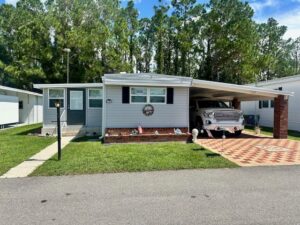 A charming, single-story house at 184 Lakeside Ranch Drive features a carport and parked truck, nestled among trees. The front lawn boasts ornamental decorations, while the driveway showcases a checkered pattern.